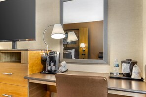A hotel room with a wooden desk, a coffee maker, a lamp, a mirror, and a television. - Best Western Queens Gold Coast (Bayside)