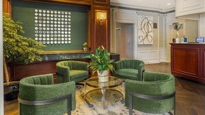 A lobby with green upholstered chairs, a glass coffee table, a decorative wall with circular patterns, and a reception desk. - Best Western Queens Gold Coast (Bayside)