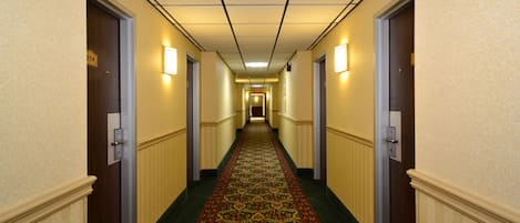 Un pasillo de hotel con alfombra estampada, puertas a ambos lados y luces en la pared.