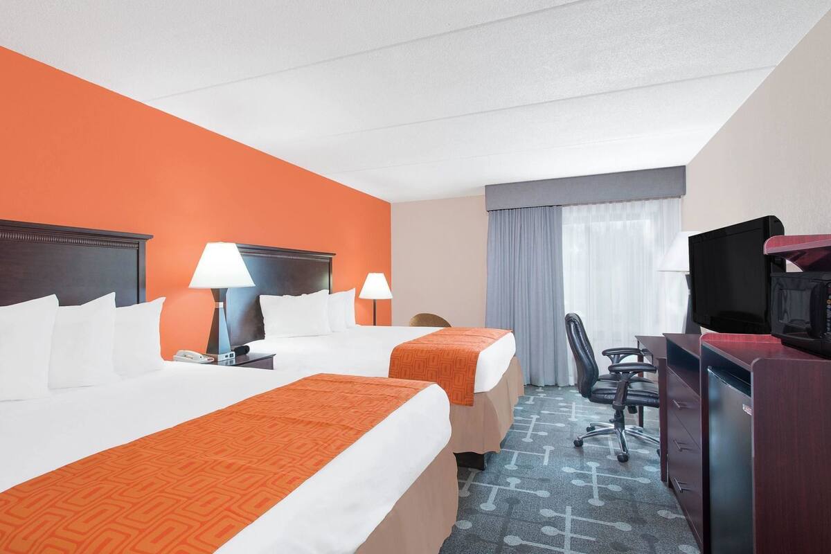 A hotel room with two beds, a desk with a television, and a chair.