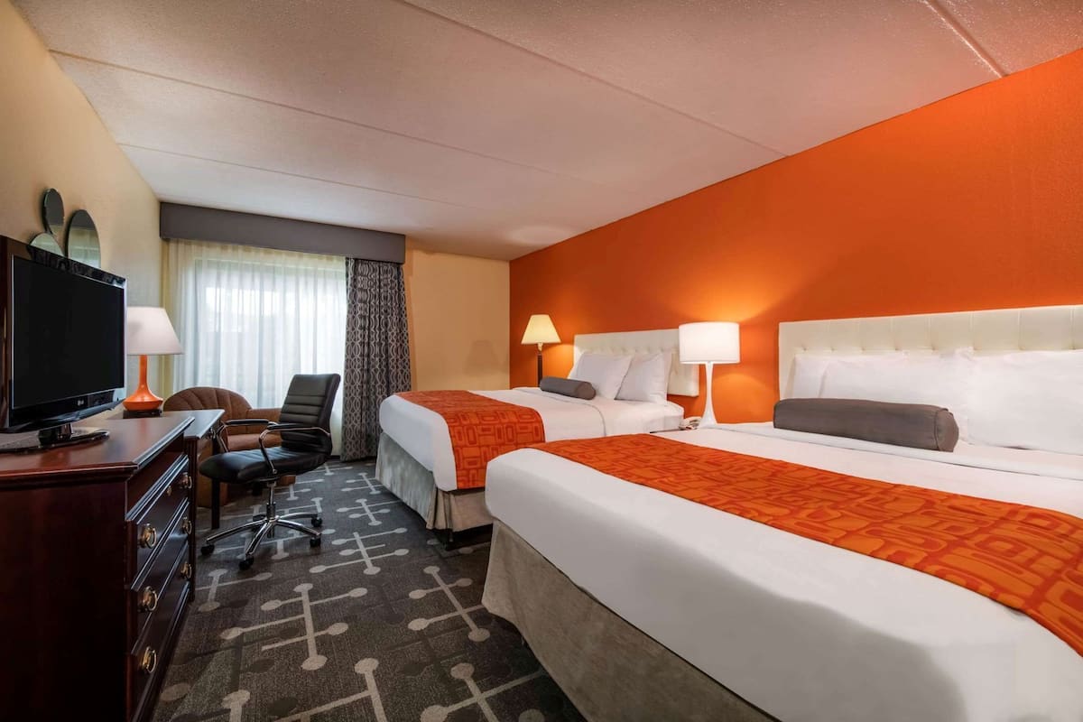 A hotel room with two beds, a desk with a TV, a chair, and a patterned carpet.
