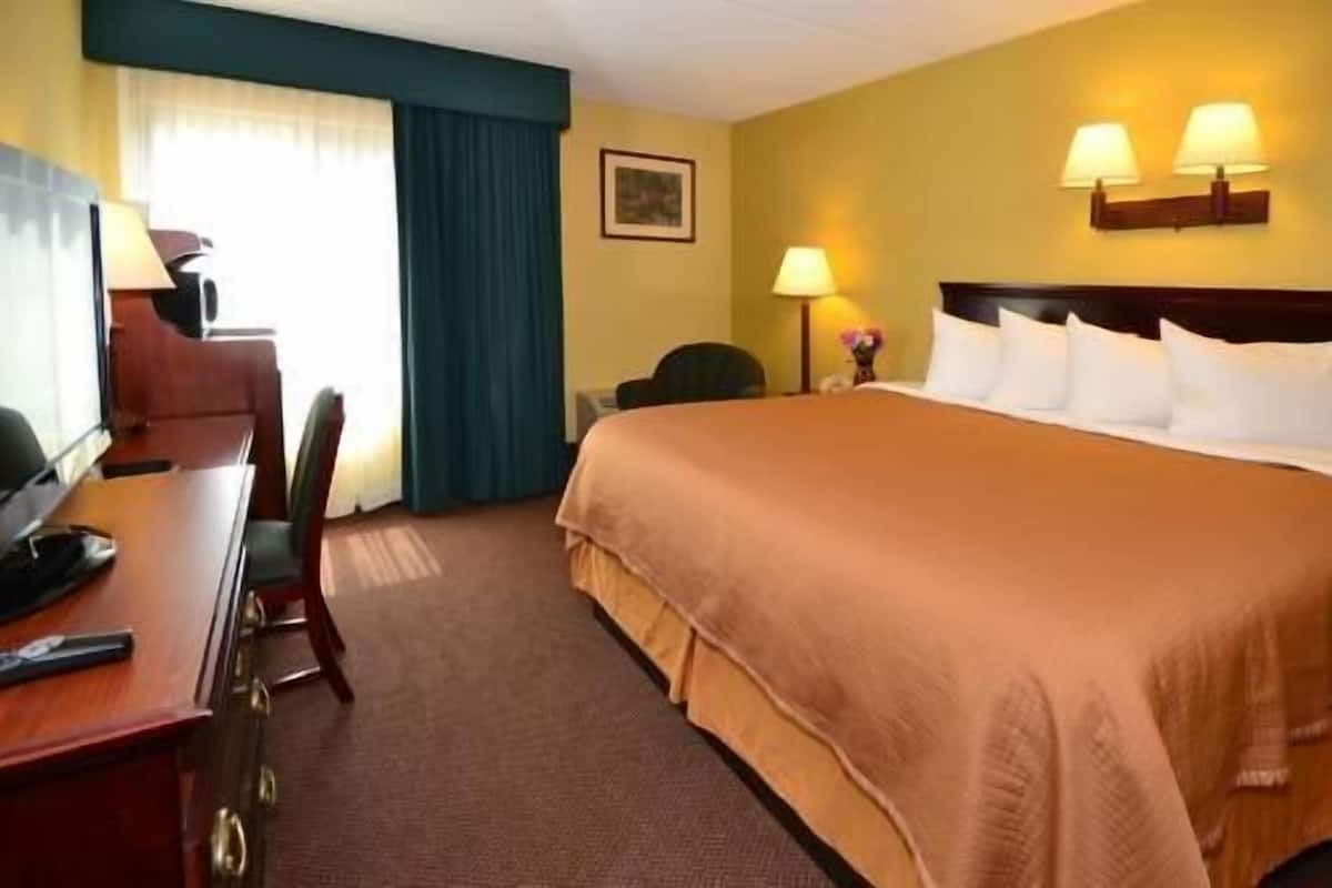 A hotel room with a bed, desk, chair, lamps, and a window with curtains.