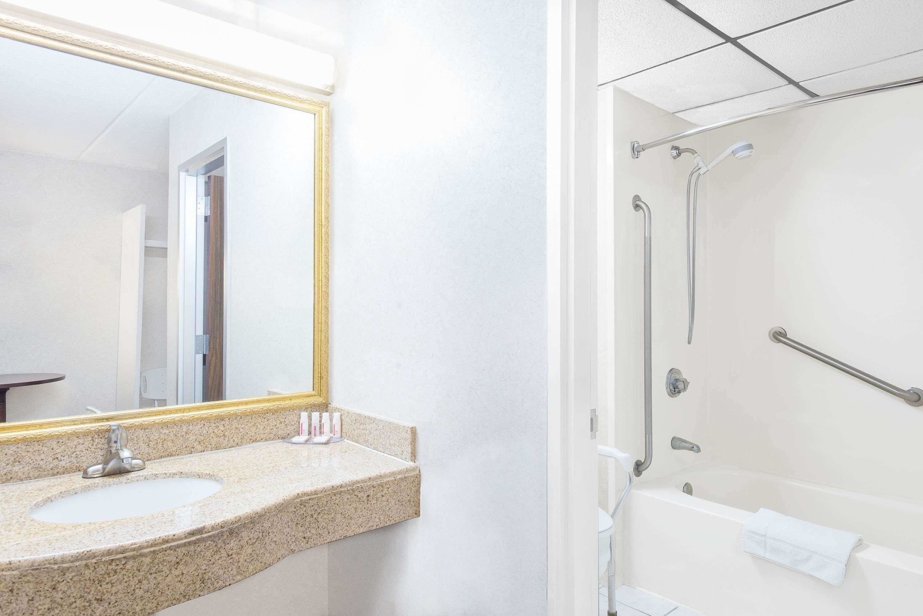 A bathroom with a granite countertop sink, a large mirror, and a walk-in shower with grab bars.