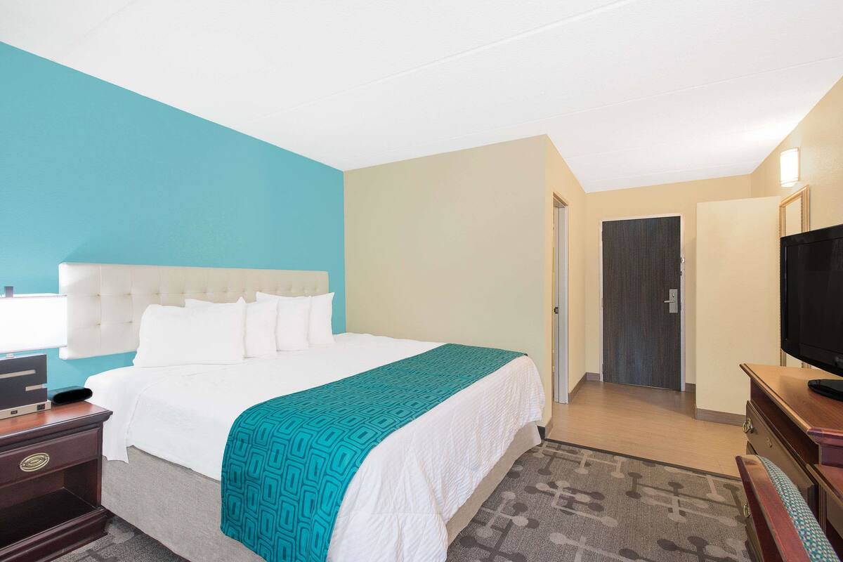 Habitación de hotel con una cama grande, televisión, escritorio con lámpara y puerta que da a otra habitación.