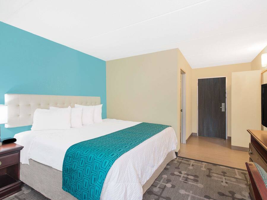 Habitación de hotel con una cama grande, televisión, escritorio con lámpara y puerta que da a otra habitación.