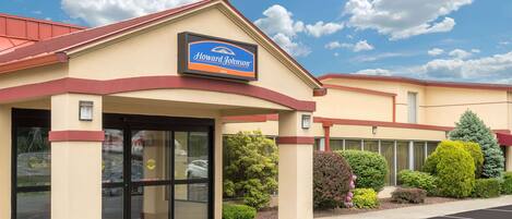 Un hotel Howard Johnson con fachada color beige, detalles en rojo y un cielo azul despejado con nubes.