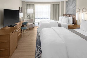 Habitación de hotel con dos camas, televisión, escritorio, silla y lámpara.