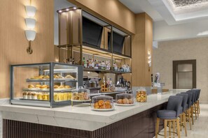 Una barra de desayuno con pasteles, una estación de café y una zona de bar con botellas.