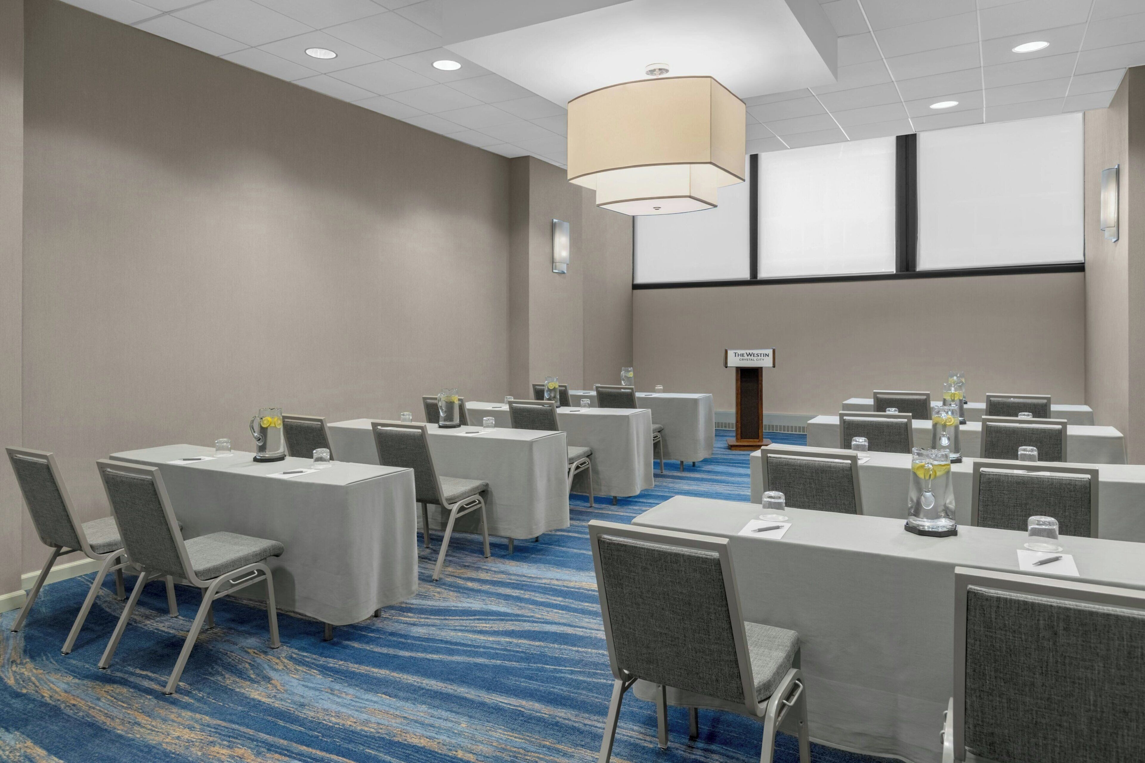 Un salón de conferencias con varias mesas, sillas y una pantalla grande al frente.