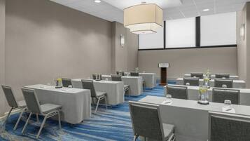Un salón de conferencias con varias mesas, sillas y una pantalla grande al frente.