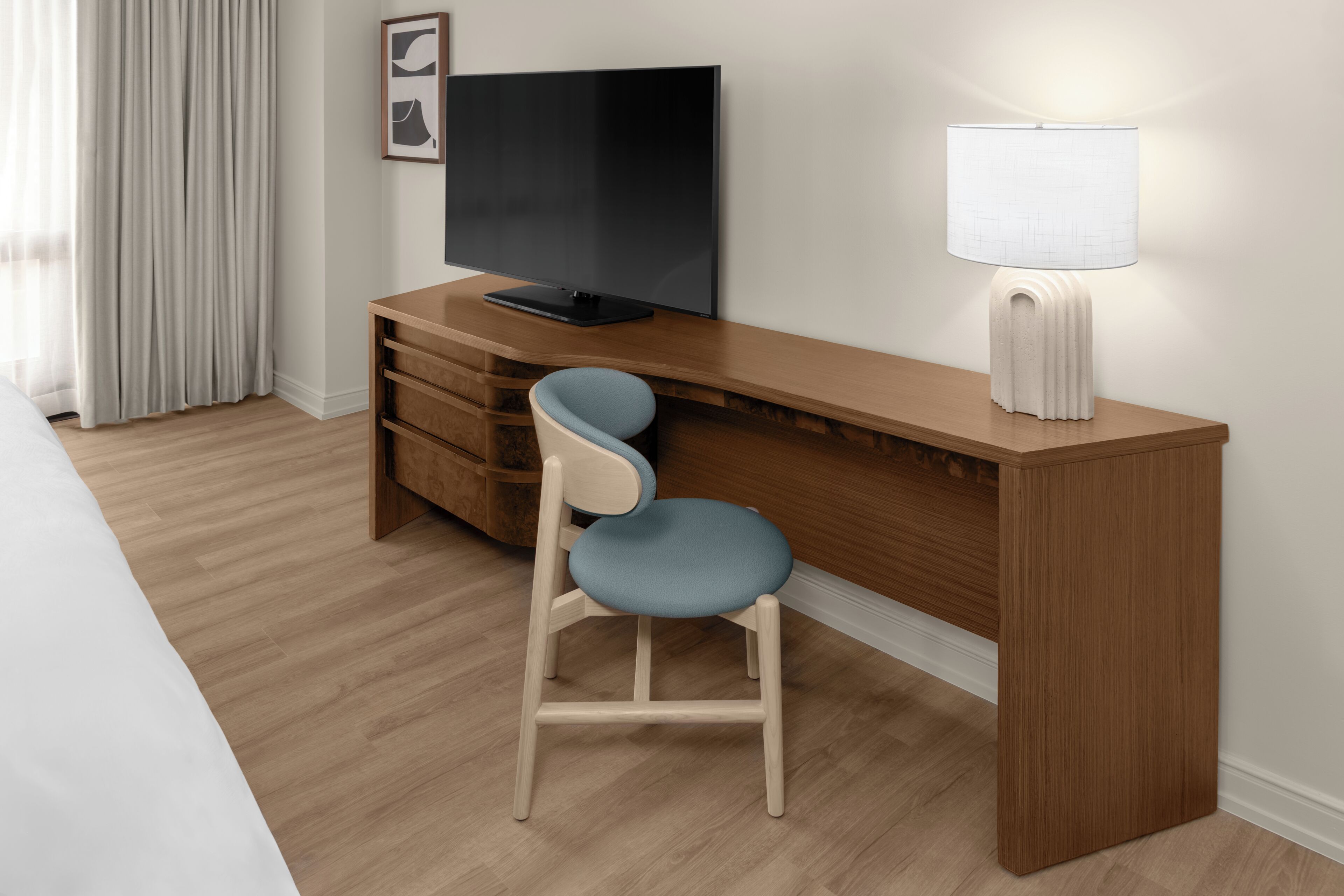 A hotel room with a wooden desk, a television, a lamp, and a blue chair.