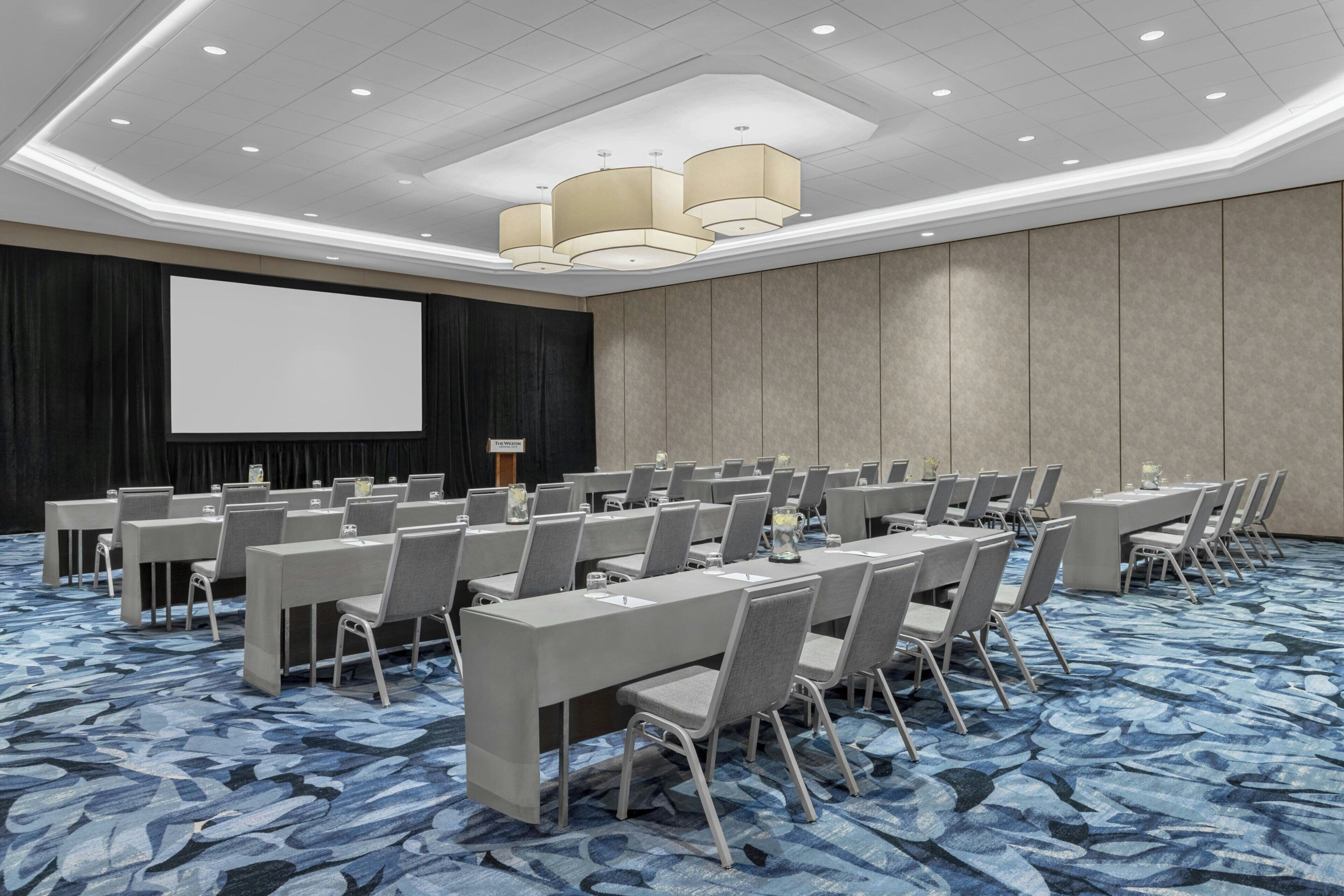 Une salle de conférence équipée d’un grand écran, de plusieurs tables et de chaises disposées pour une réunion.