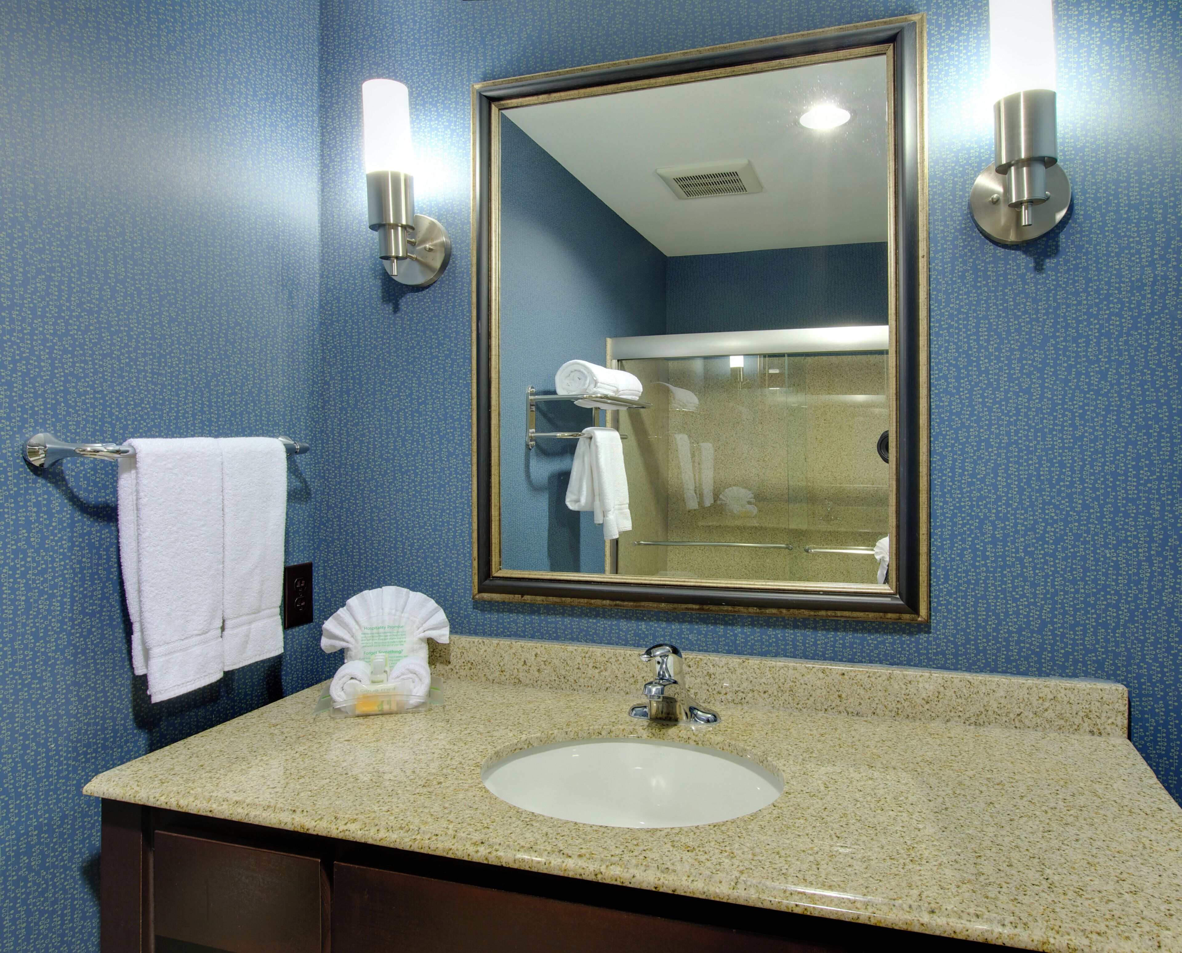 A bathroom with a sink, mirror, towel rack, and a glass shower door.