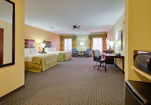 A hotel room with two beds, a desk, a chair, a TV, and a ceiling fan.