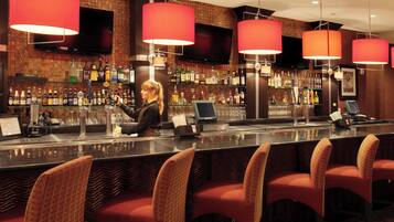 A bar area with a bartender, red chairs, and a variety of liquor bottles.