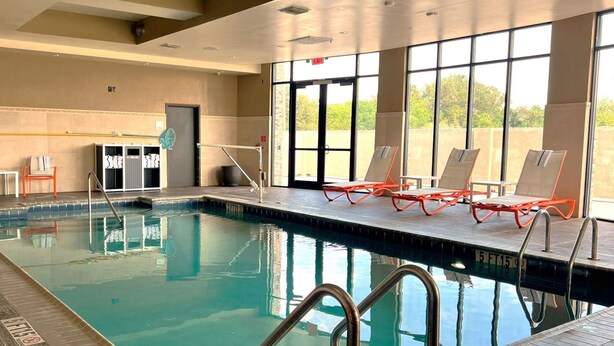 An indoor swimming pool with clear water, surrounded by lounge chairs and a sunbed area.