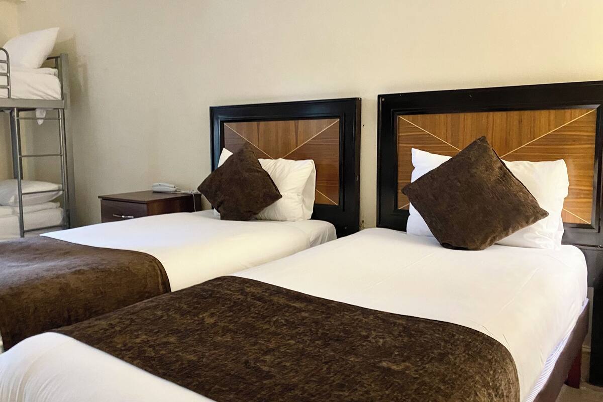 A hotel room with two single beds, a bunk bed, a bedside table with a phone, and a nightstand.