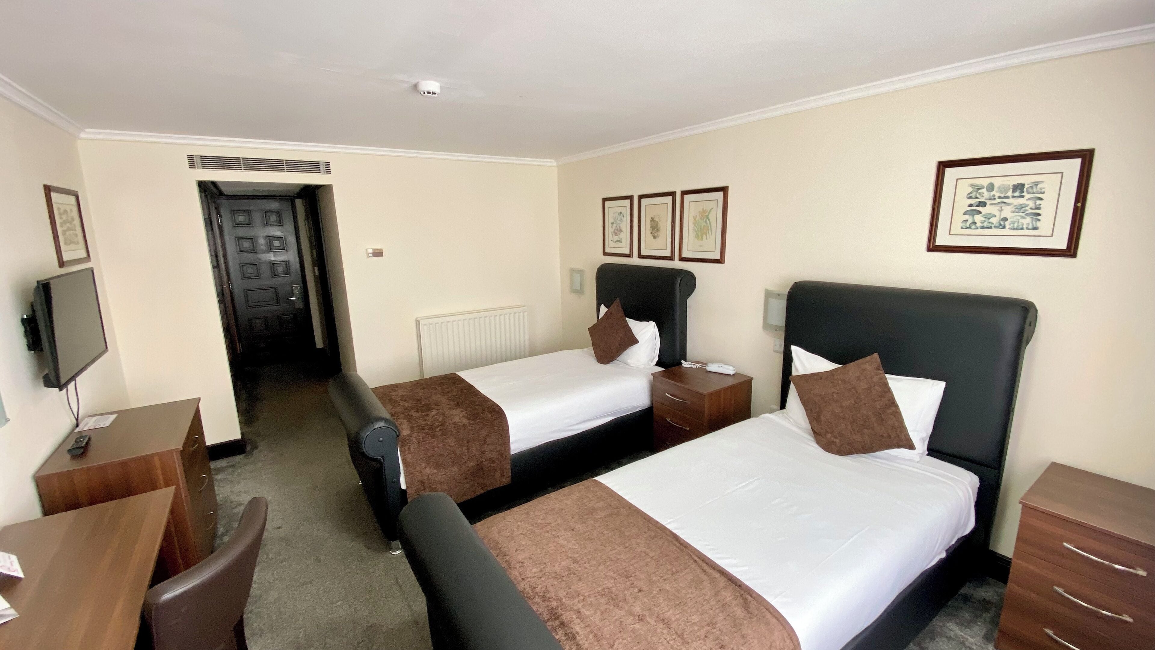 A hotel room with two beds, a desk, a chair, a TV, and framed pictures on the wall.