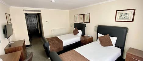 A hotel room with two beds, a desk, a chair, a TV, and framed pictures on the wall.