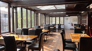 Een restaurant met meerdere tafels en stoelen, grote ramen en een betegelde vloer.