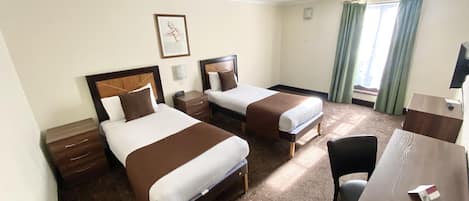 A hotel room with two beds, a desk, a chair, a TV, and a window with curtains.