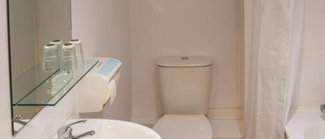 A small, modern bathroom with a white sink, toilet, and shower curtain.