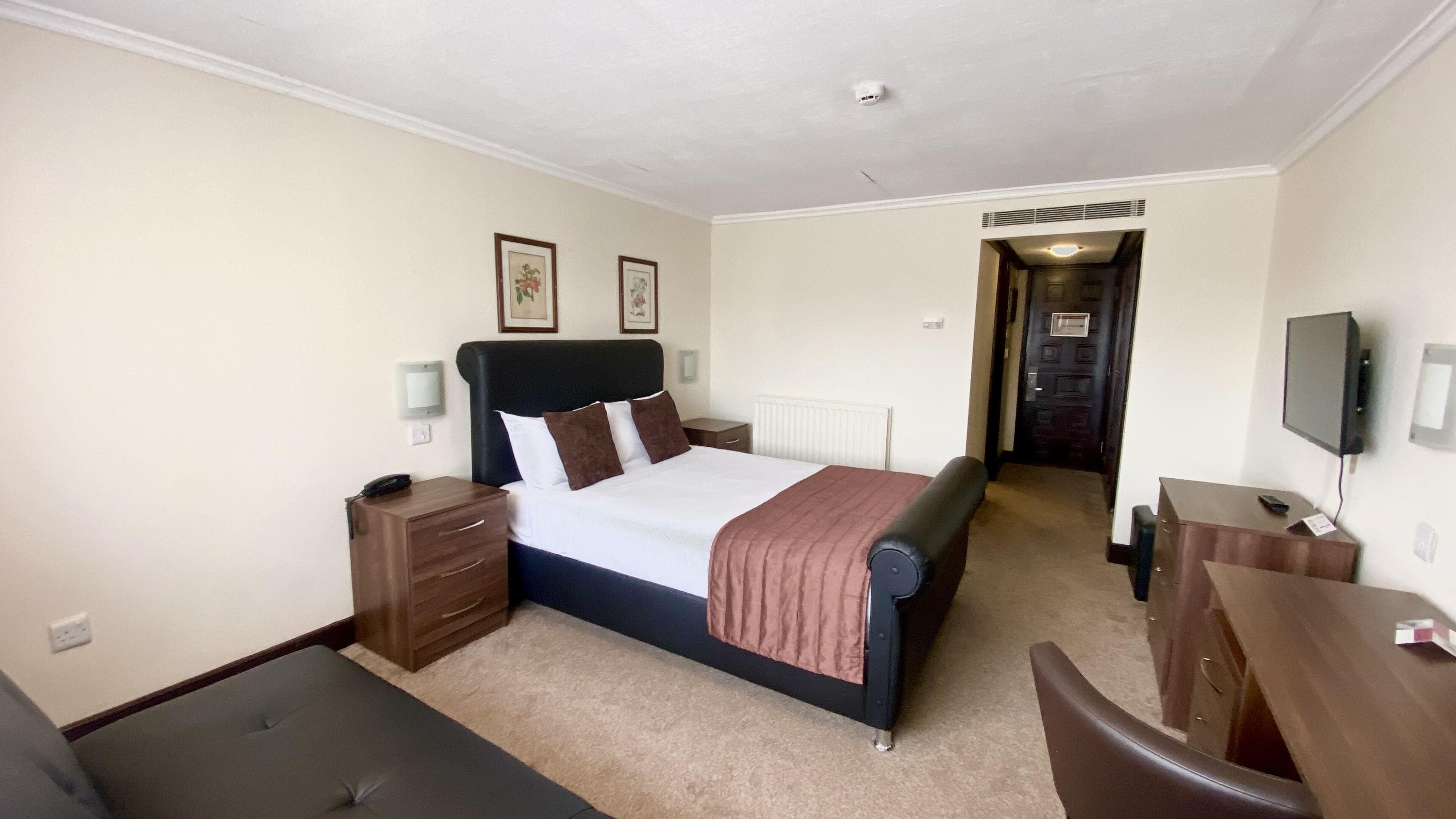 A hotel room with a bed, bedside tables, a desk, a chair, and a television.