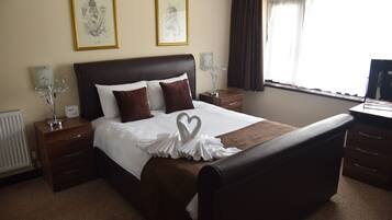 A hotel room with a large bed, two bedside tables, a nightstand, a dresser, a window with curtains, and two framed pictures on the wall.