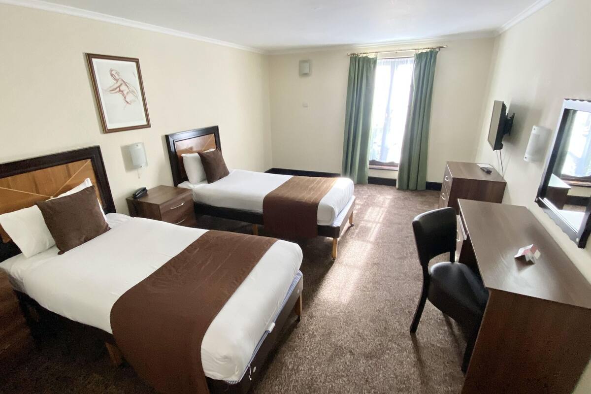A hotel room with two beds, a desk, a chair, a TV, and a window with curtains.