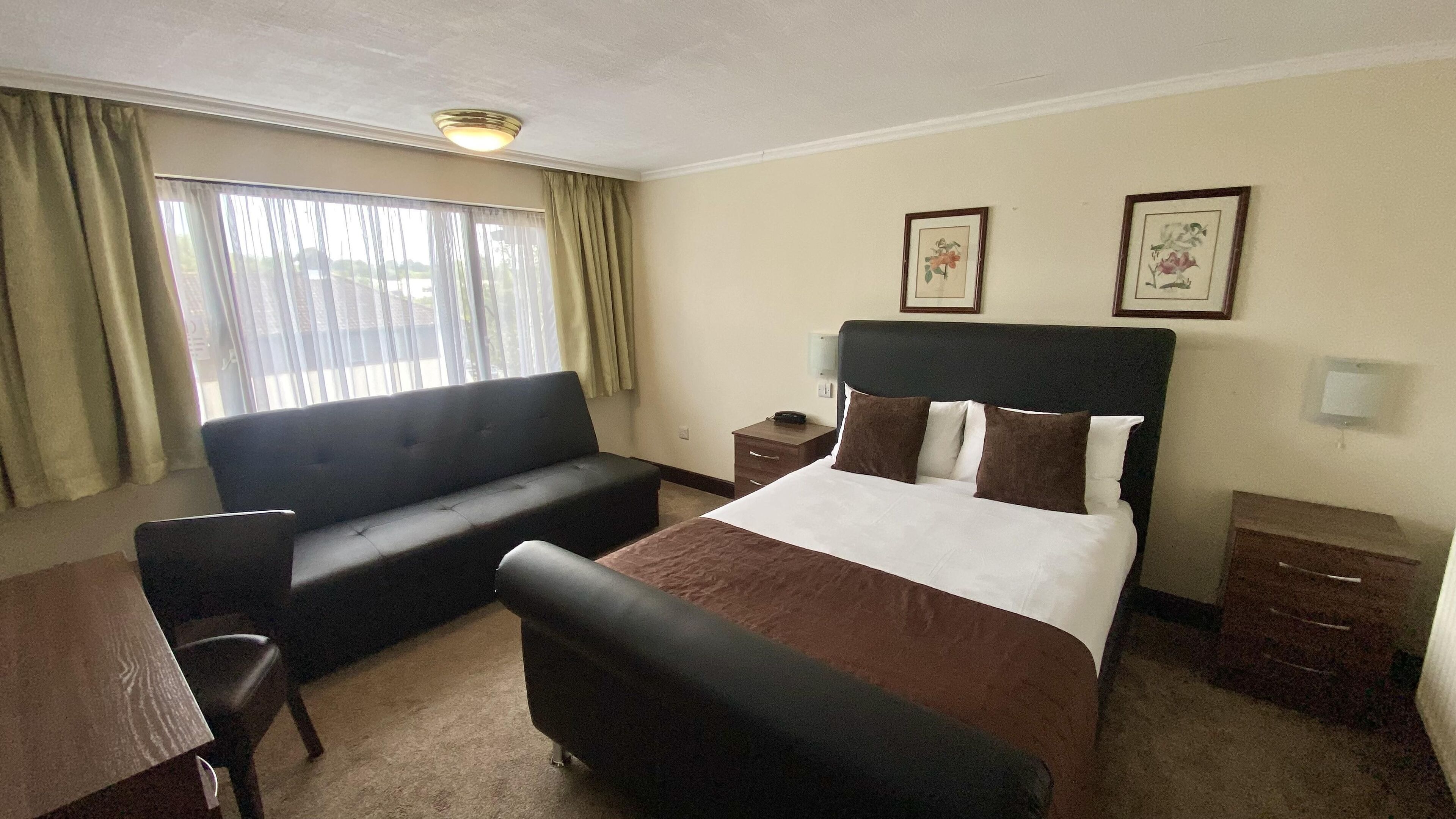Habitación de hotel con cama, sofá, escritorio y una silla. Dos cuadros enmarcados adornan la pared.