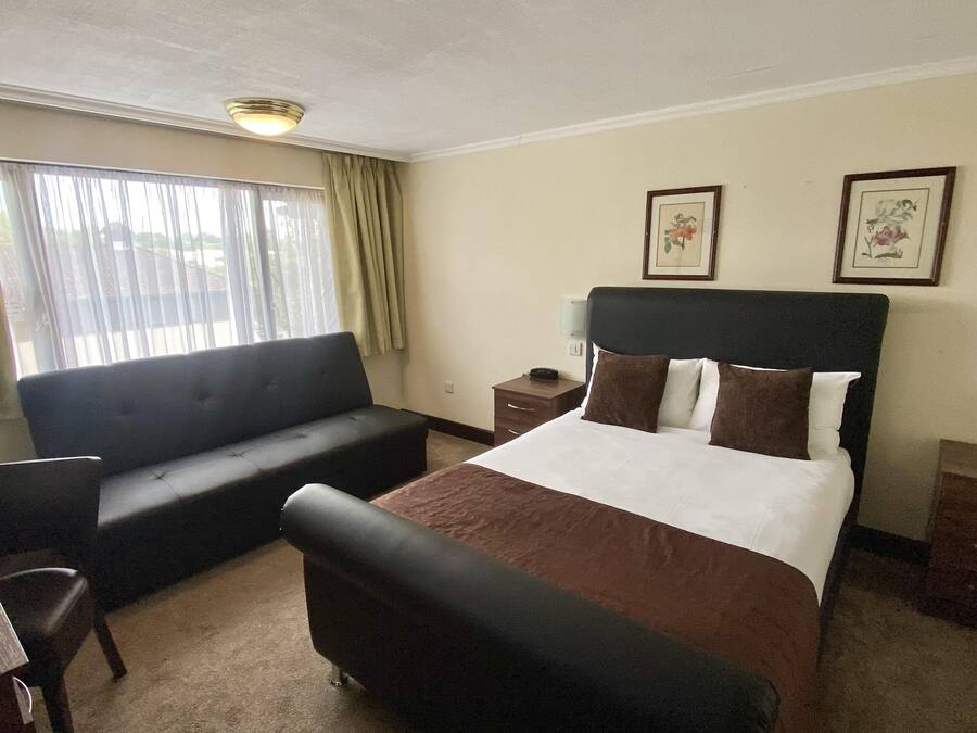 Habitación de hotel con cama, sofá, escritorio y una silla. Dos cuadros enmarcados adornan la pared.
