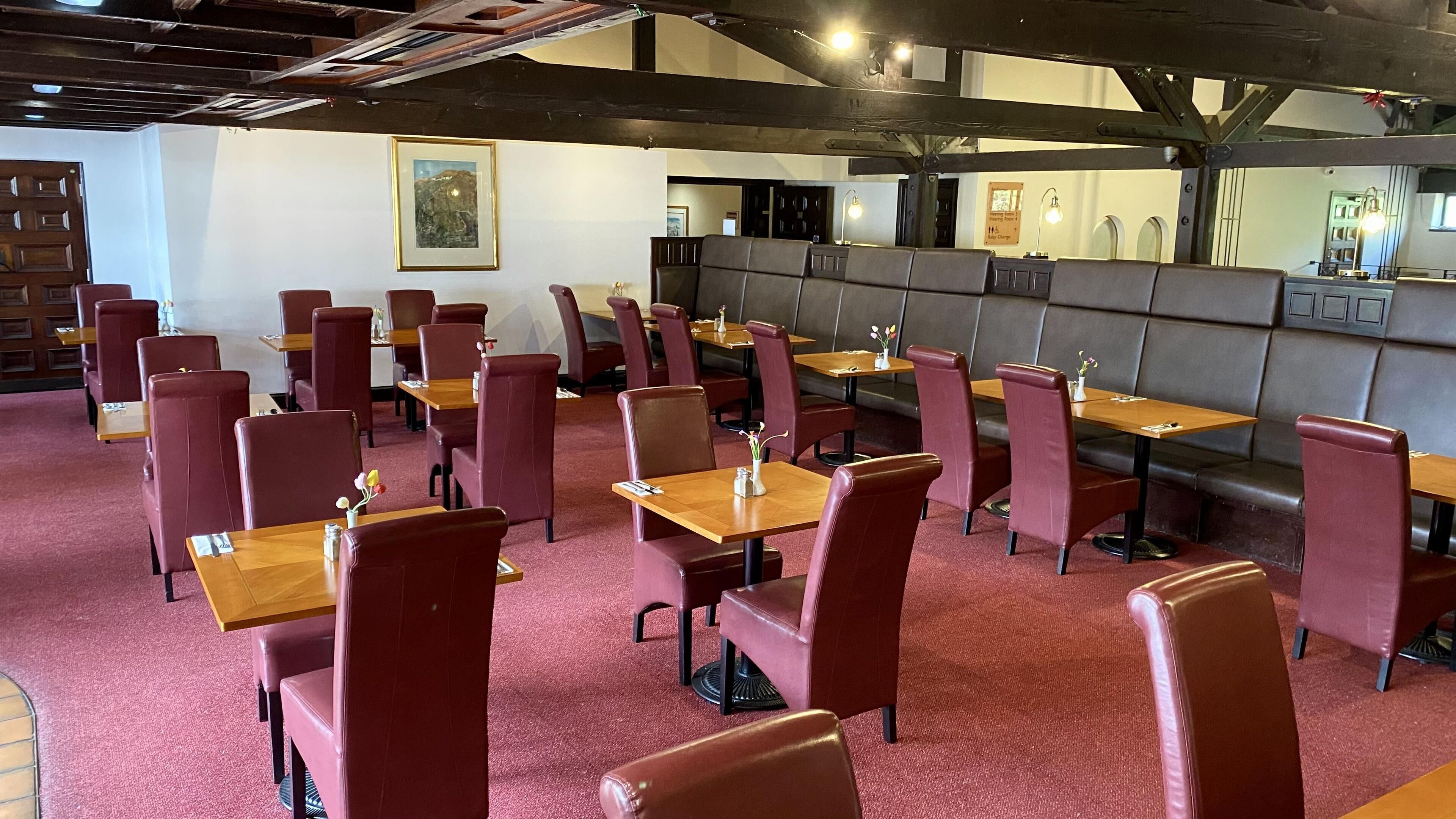 A restaurant with booths and tables, red upholstered chairs, and a red carpeted floor.