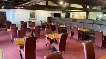 A restaurant with booths and tables, red upholstered chairs, and a red carpeted floor.