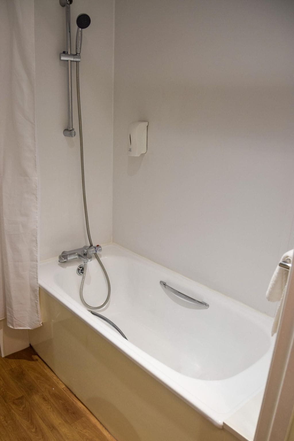 A bathroom with a white bathtub, a handheld showerhead, and a wall-mounted faucet.