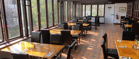 A restaurant with multiple tables and chairs, large windows, and a tiled floor.