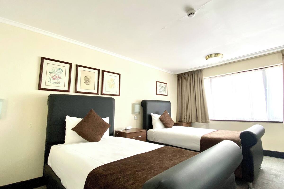 A hotel room with two beds, a desk, a chair, and a window with curtains.