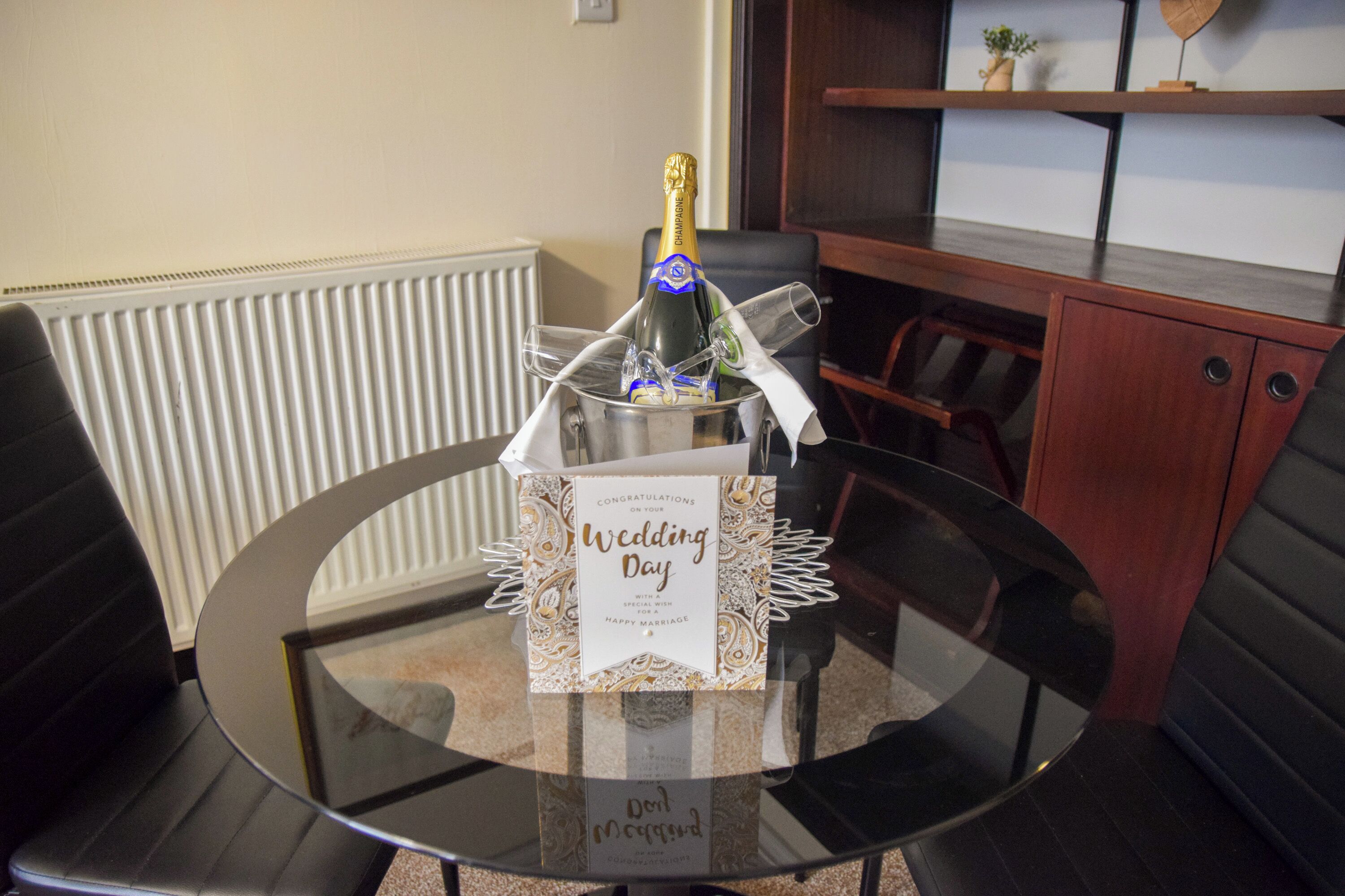 A glass table with a bottle of champagne, a glass, and a wedding day card.