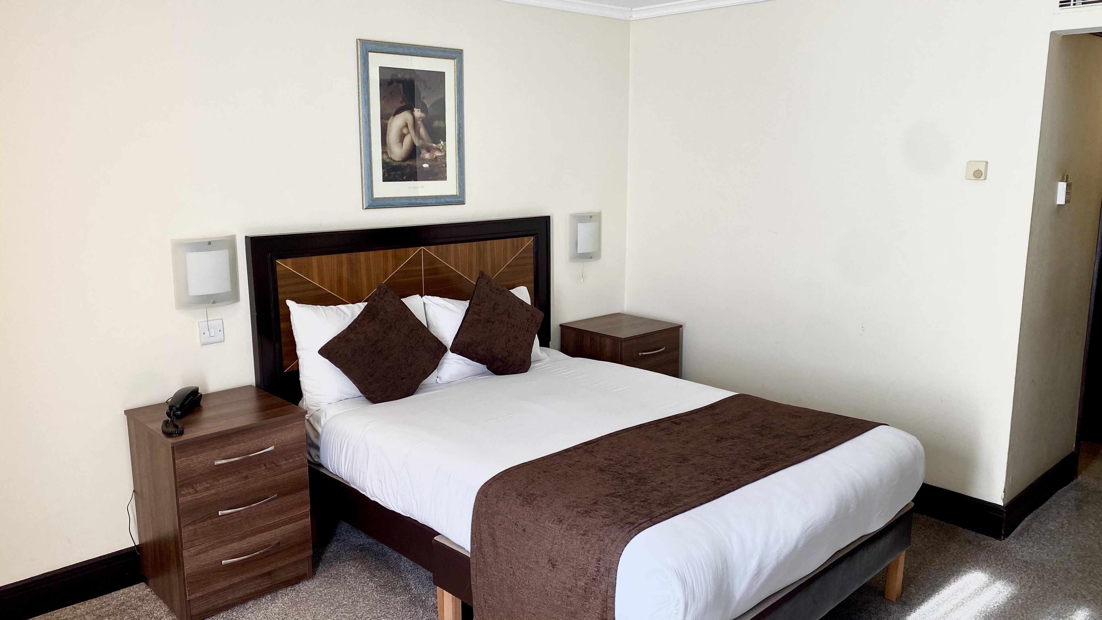 A neatly made bed with a brown headboard, white bedding, and two nightstands with drawers.