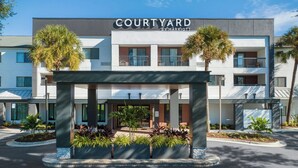 Ein Courtyard by Marriott Hotel mit überdachter Eingangspartei, Palmen und einer modernen Fassade.