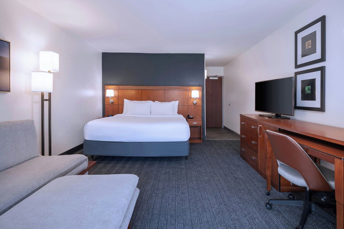 A hotel room with a large bed, a desk with a chair, a flat-screen TV, and a sofa.