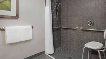 A shower area with a white shower curtain, a grab bar, and a white plastic stool.