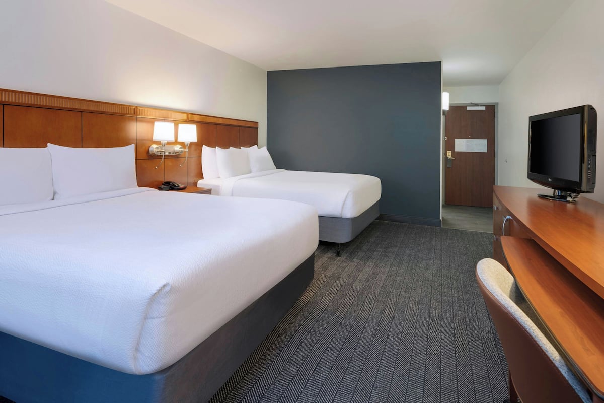 Une chambre d’hôtel avec deux lits, un bureau avec une télévision et une porte visible au fond.