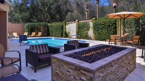 Ein Poolbereich mit Liegestühlen, einer Feuerstelle und einem Sonnenschirm.