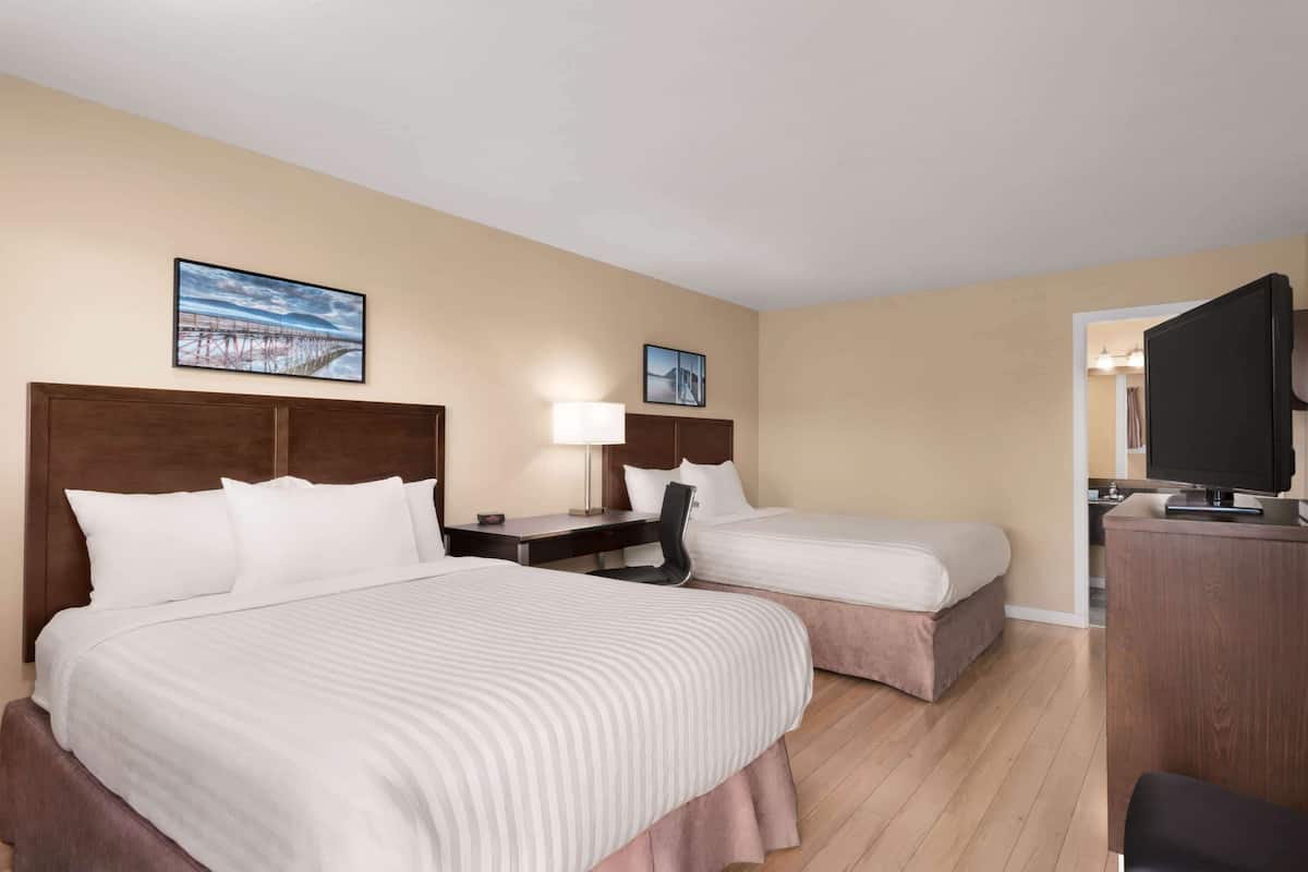 Une chambre d’hôtel avec deux lits, un bureau, une chaise, une télévision et un tableau au mur.