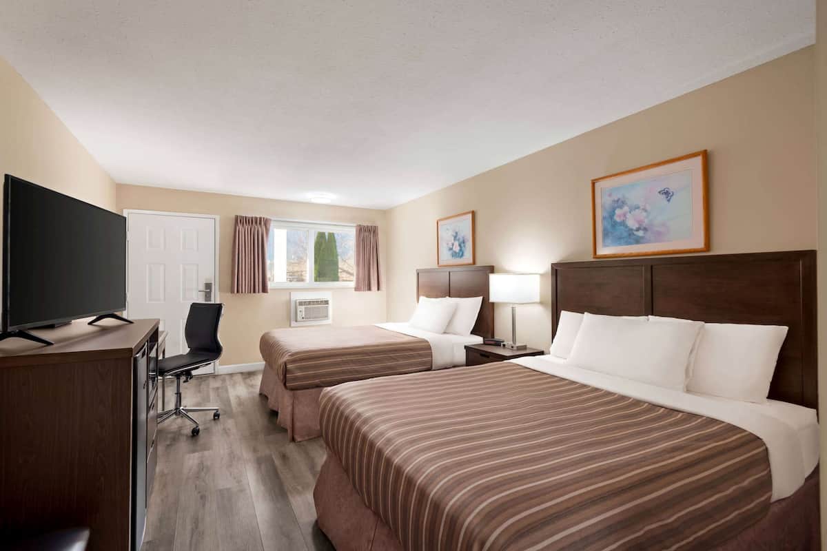 Une chambre d’hôtel avec deux lits, un bureau doté d’un téléviseur à écran plat, une chaise, une lampe de bureau et des œuvres d’art encadrées accrochées au mur.