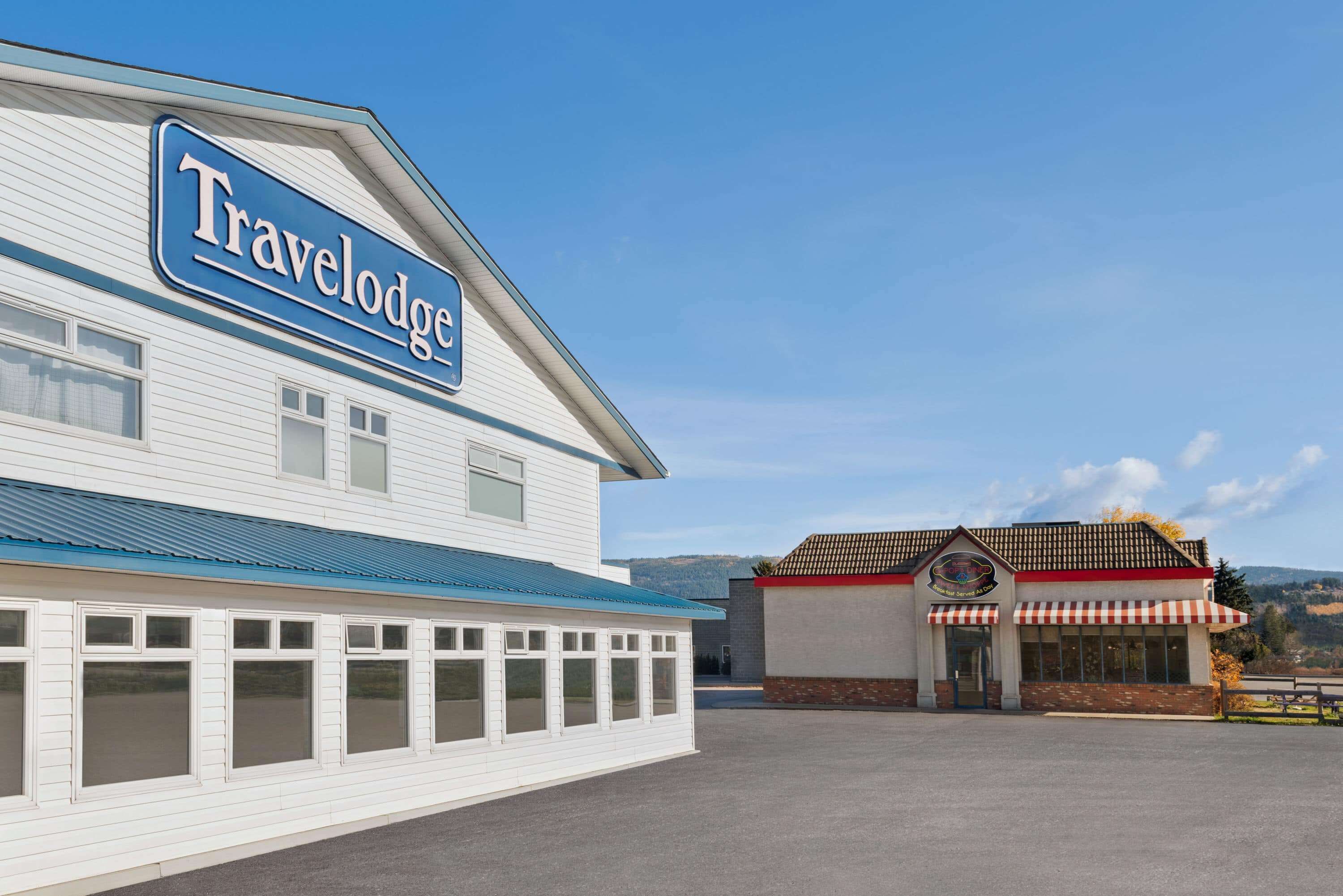 A Travelodge building with a blue awning and a red and white striped awning restaurant in the background.