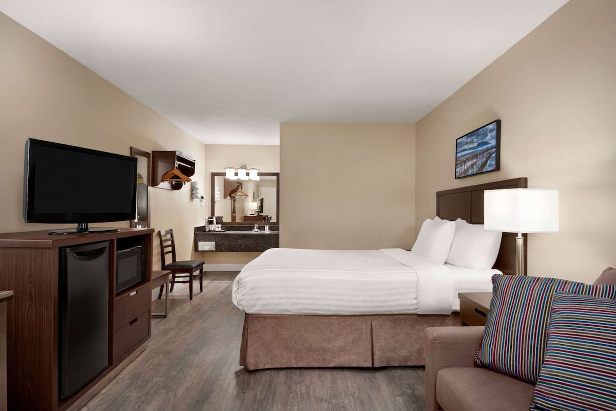 Une chambre d’hôtel avec un lit, une télévision, un bureau avec un ordinateur, une chaise, une commode et une salle de bain visible au fond.