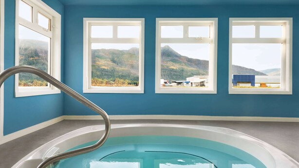 Une chambre dotée d’une grande baignoire, de trois fenêtres offrant une vue sur les montagnes et d’une main courante en métal.