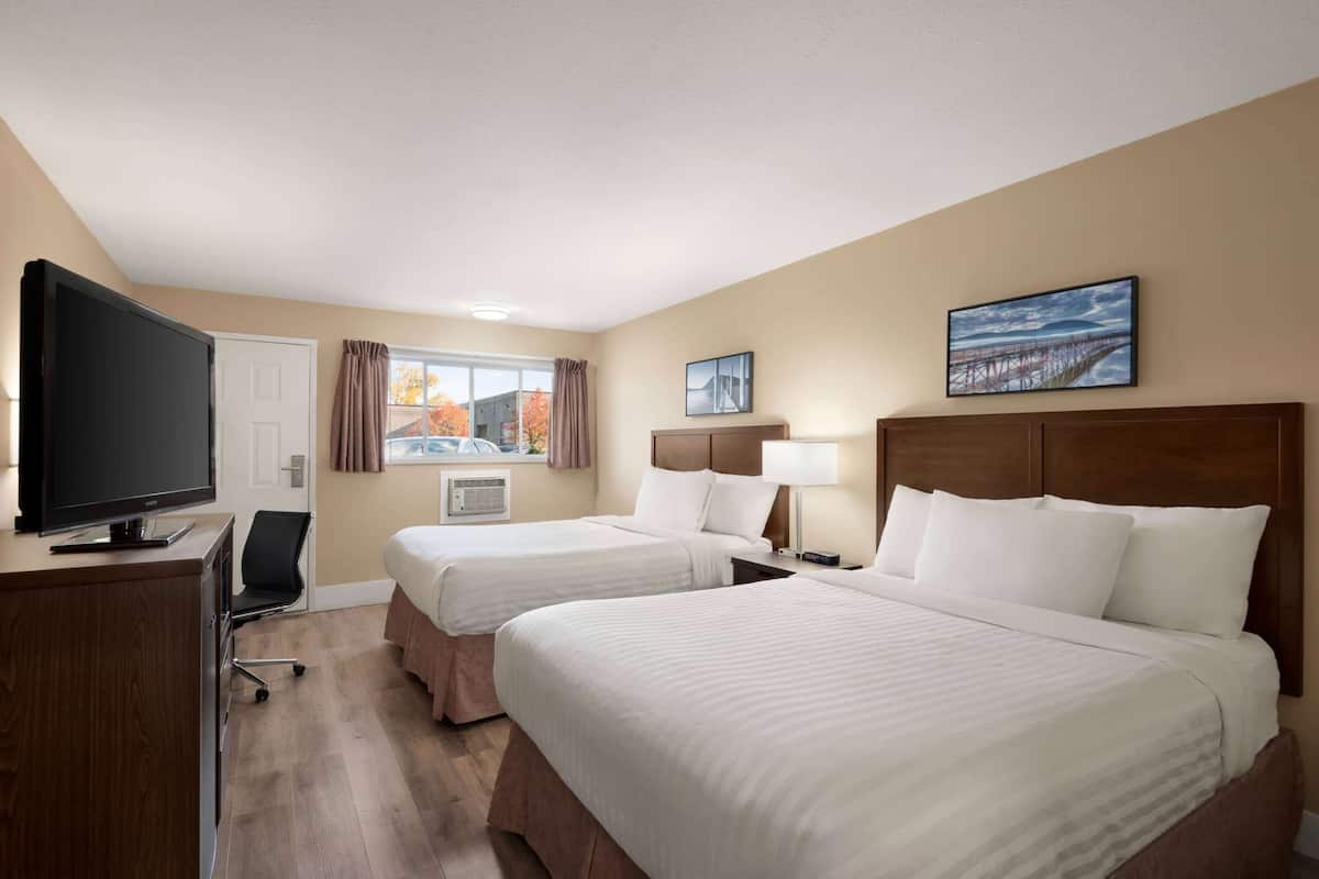 Une chambre d’hôtel avec deux lits, une télévision, un bureau et une fenêtre donnant sur des immeubles et des arbres.