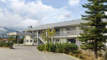 A motel with a two-story structure, a covered parking area, and a mountain backdrop.